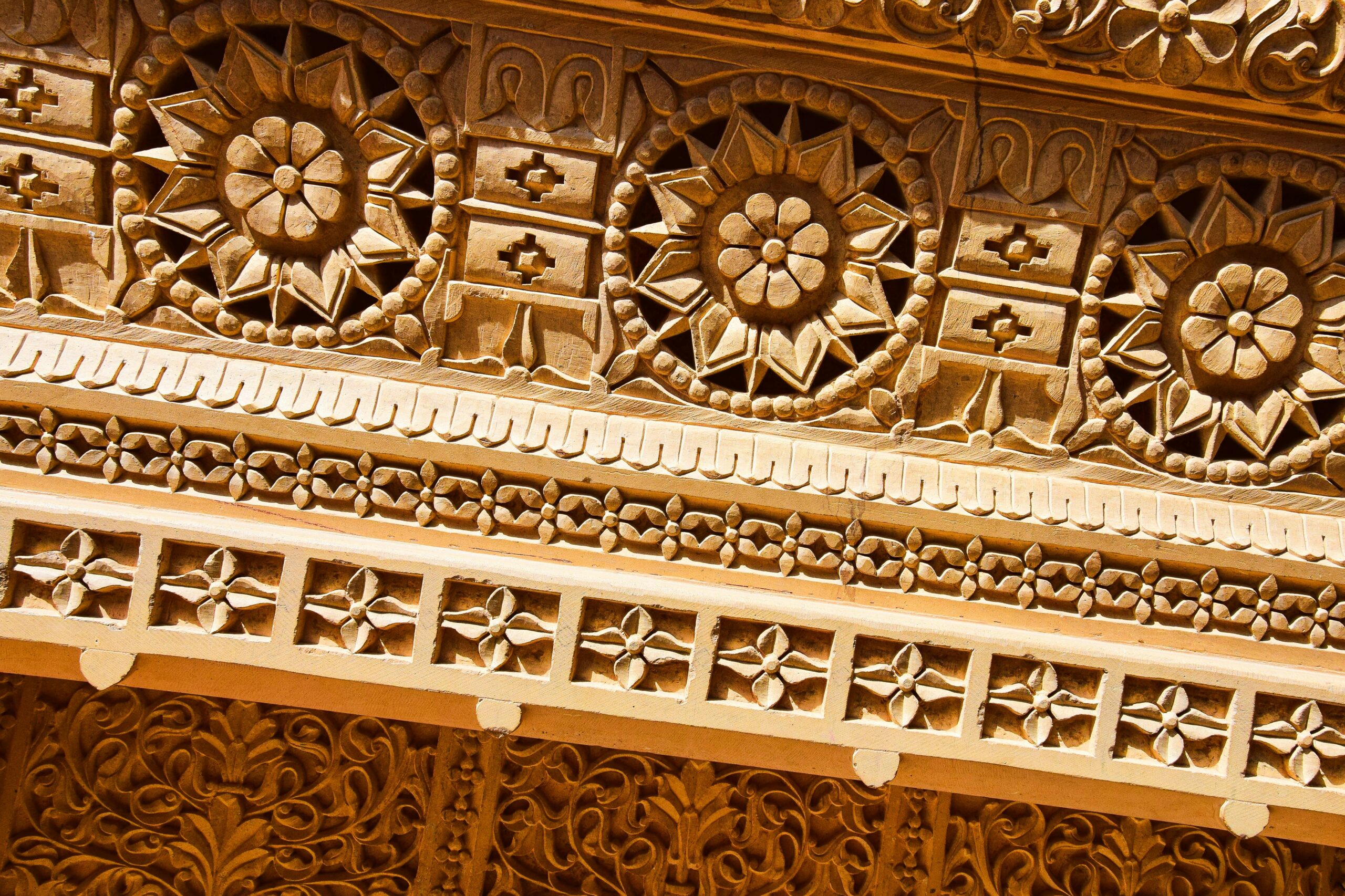 Detailed close-up of sunlit ornamental carvings on Indian sandstone wall.
